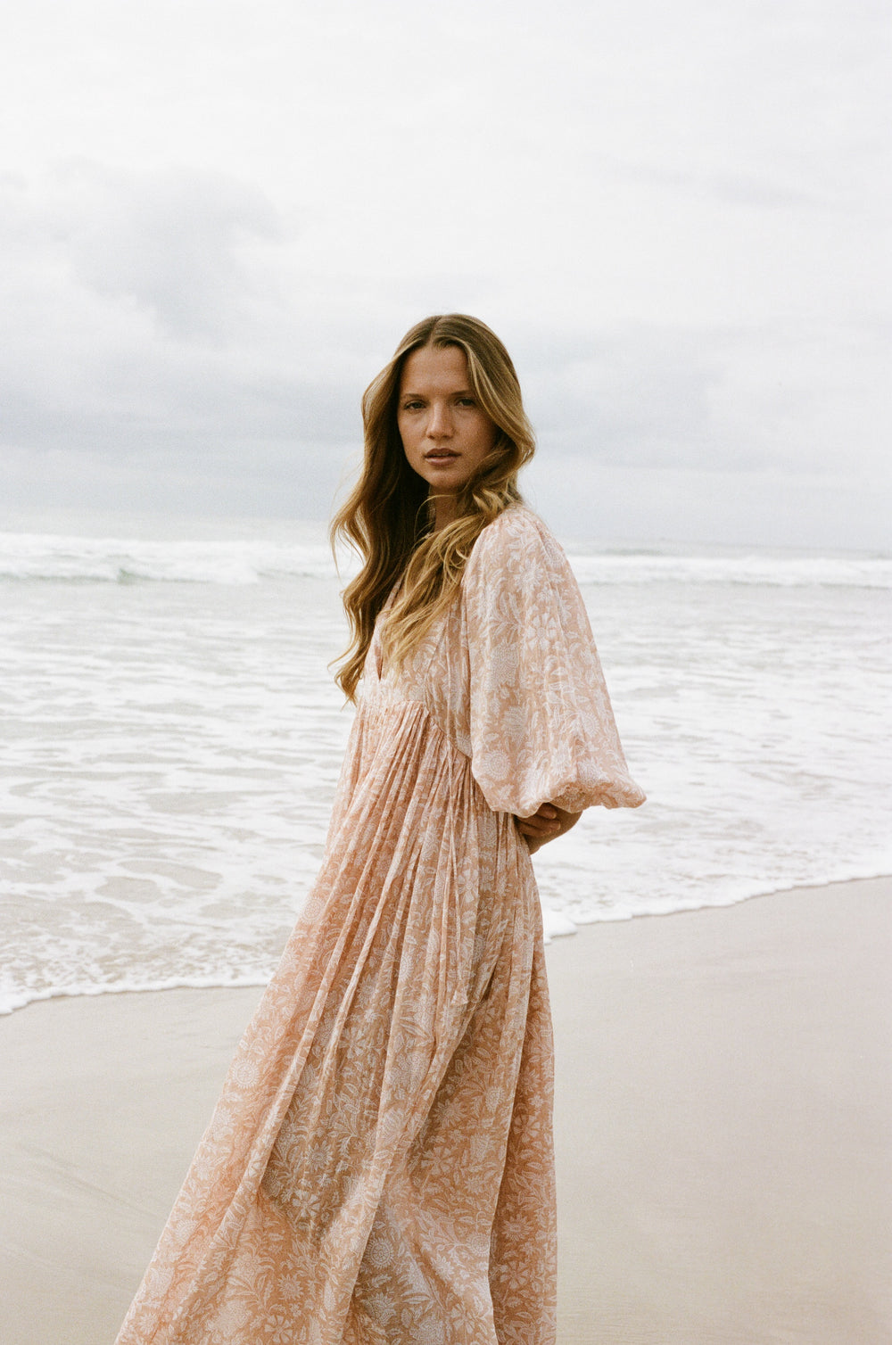 Daughters of India Kyra Maxi Dress in Apricot Blush — walking on beach, V-neckline and billowed sleeves in ocean breeze