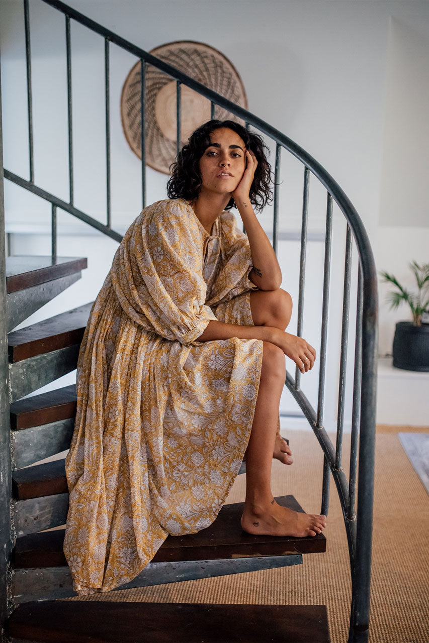 Daughters of India Kyra Midi Dress in Cumin — seated on spiral staircase, hand on cheek, relaxed pose