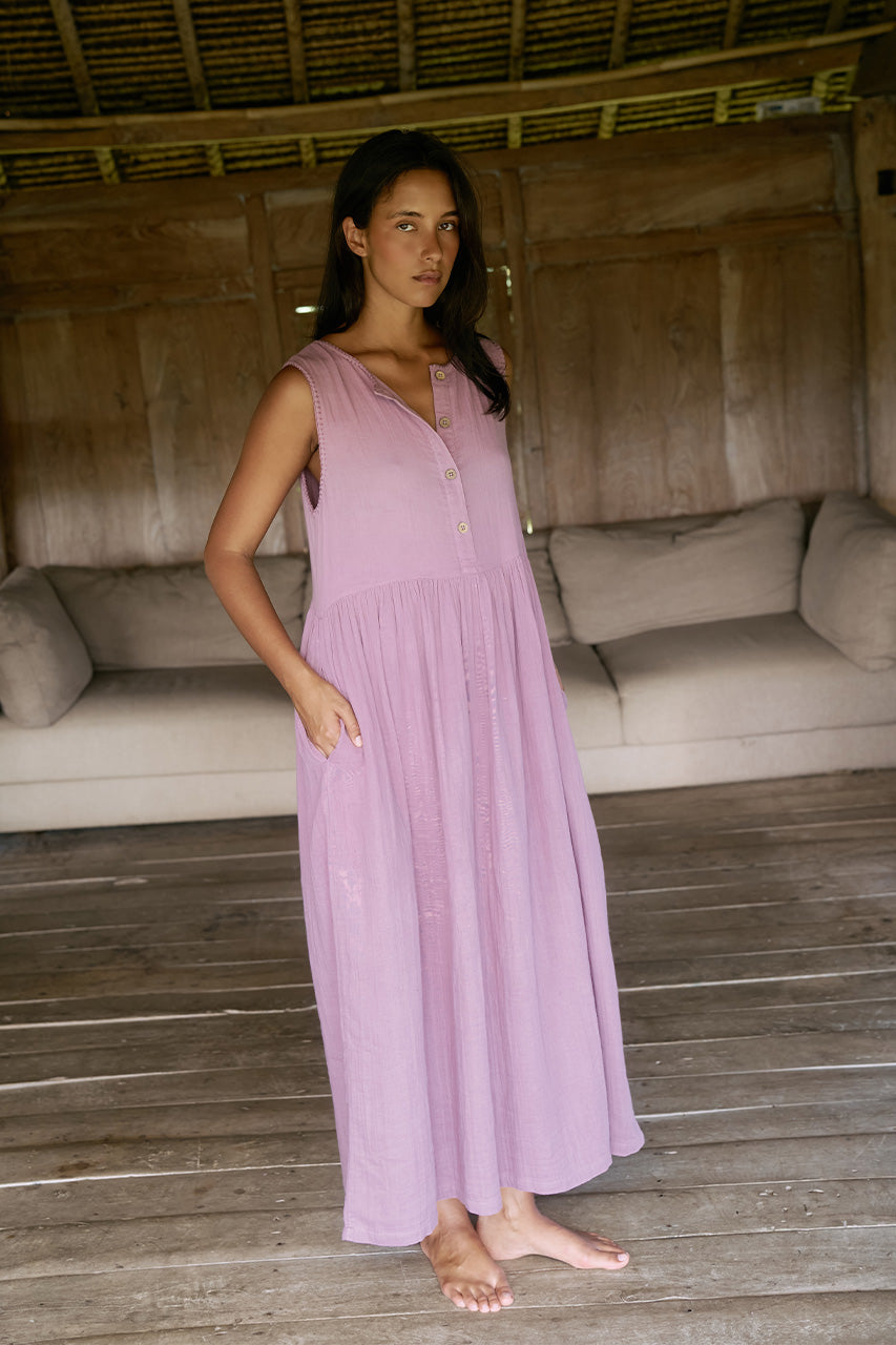 Nadi Dress Mauve — full length front angle view on wooden floorboards, mauve double gauze cotton midi dress with wooden button front and flowing gathered skirt, rustic bamboo lounge interior | Daughters of India